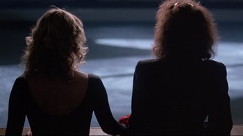Movie still from “Flashdance” (1983), directed by Adrian Lyne – Two women sitting next to each other holding hands; Medium shot, Over the shoulder angle