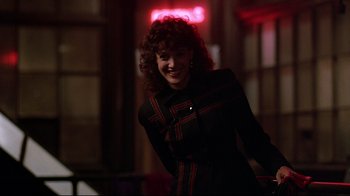 Movie still from “Flashdance” (1983), directed by Adrian Lyne – A woman with curly red hair smiling for the camera; Medium shot, Over the shoulder angle