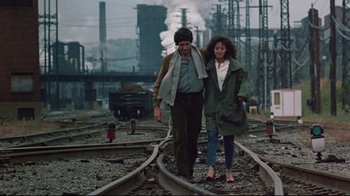 Movie still from “Flashdance” (1983), directed by Adrian Lyne – A man and a woman are walking on train tracks; Wide shot, High angle
