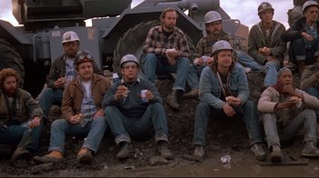 Movie still from “Flashdance” (1983), directed by Adrian Lyne – A group of men sitting next to each other on top of a hill; Wide shot, High angle