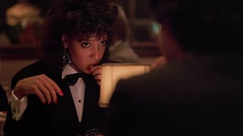A woman in a suit and bow tie holding a blow dryer to her mouth