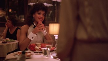Movie still from “Flashdance” (1983), directed by Adrian Lyne – A woman sitting at a table with a glass of wine; Medium shot, Over the shoulder angle