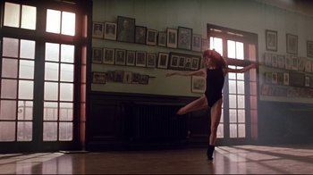 Movie still from “Flashdance” (1983), directed by Adrian Lyne – A woman in black leotard doing a dance move in a room; Wide shot, Low angle