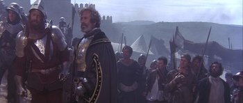 Movie still from “Flesh+Blood” (1985), directed by Paul Verhoeven – A group of people in medieval garb in a field; Medium shot, Over the shoulder angle