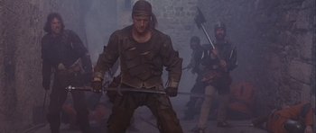 Movie still from “Flesh+Blood” (1985), directed by Paul Verhoeven – A group of men in medieval garb holding swords; Medium shot, Low angle
