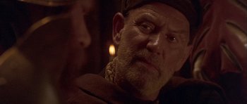 Movie still from “Flesh+Blood” (1985), directed by Paul Verhoeven – An older man with a beard and a hat; Close Up shot, Over the shoulder angle