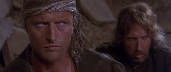 Movie still from “Flesh+Blood” (1985), directed by Paul Verhoeven – A person with a snake skin head wrap; Close Up shot, Over the shoulder angle