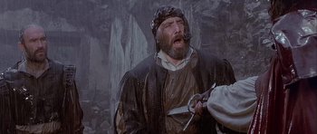 Movie still from “Flesh+Blood” (1985), directed by Paul Verhoeven – An old man with a long beard holding a pair of shears; Medium shot, Low angle