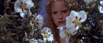 Movie still from “Flesh+Blood” (1985), directed by Paul Verhoeven – A young woman looking at the camera through flowers; Close Up shot, Low angle