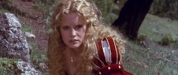 Movie still from “Flesh+Blood” (1985), directed by Paul Verhoeven – A woman with long blonde curly hair wearing a red hat; Close Up shot, Low angle