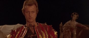 Movie still from “Flesh+Blood” (1985), directed by Paul Verhoeven – A person wearing a red and gold costume; Close Up shot, Over the shoulder angle