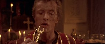 Movie still from “Flesh+Blood” (1985), directed by Paul Verhoeven – A man in a red and gold jacket eating a fork; Close Up shot, High angle