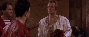 Movie still from “Flesh+Blood” (1985), directed by Paul Verhoeven – A man wearing a white shirt and a gold chain; Medium shot, Over the shoulder angle