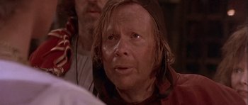 Movie still from “Flesh+Blood” (1985), directed by Paul Verhoeven – A man with a beard and a hat on looking at the camera; Close Up shot, Over the shoulder angle