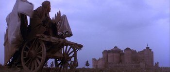 Movie still from “Flesh+Blood” (1985), directed by Paul Verhoeven – An image of a man sitting in a wagon in front of a castle; Wide shot, Low angle