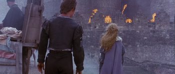 Movie still from “Flesh+Blood” (1985), directed by Paul Verhoeven – A man and a woman standing in front of a burning building; Wide shot, Low angle