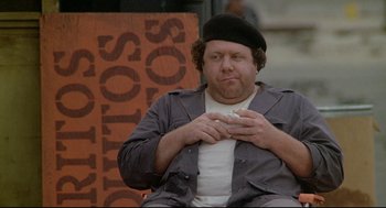 Movie still from “Fletch” (1985), directed by Michael Ritchie – A man sitting on a chair with a cigarette in his mouth; Close Up shot, High angle