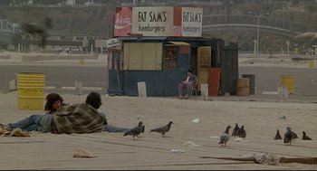 Movie still from “Fletch” (1985), directed by Michael Ritchie – A man sitting on the ground next to a group of pigeons; Wide shot, High angle