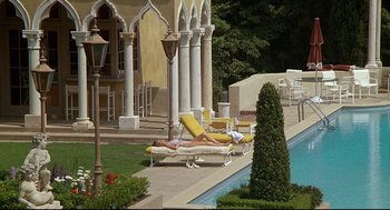 Movie still from “Fletch” (1985), directed by Michael Ritchie – Two people are laying on lounge chairs near a pool; Extreme Wide shot, High angle