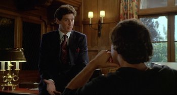 Movie still from “Fletch” (1985), directed by Michael Ritchie – A man in a suit and tie talking to another man in a suit and tie; Medium shot, Over the shoulder angle