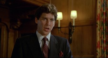 Movie still from “Fletch” (1985), directed by Michael Ritchie – A man wearing a suit and tie in a room; Close Up shot, Over the shoulder angle
