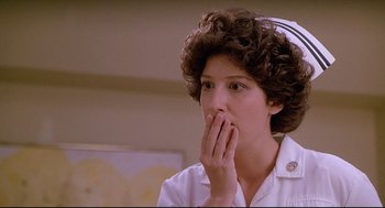 Movie still from “Fletch” (1985), directed by Michael Ritchie – A woman with curly hair is holding her hand to her mouth; Close Up shot, Low angle