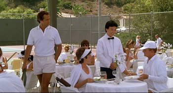 Movie still from “Fletch” (1985), directed by Michael Ritchie – A group of people sitting at a table with food; Wide shot, Over the shoulder angle