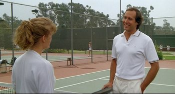 Movie still from “Fletch” (1985), directed by Michael Ritchie – A man and a woman standing next to each other on a tennis court holding rackets; Medium shot, Over the shoulder angle