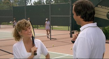 Movie still from “Fletch” (1985), directed by Michael Ritchie – A man and a woman holding tennis rackets on a tennis court; Medium shot, Over the shoulder angle