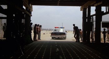 Movie still from “Fletch” (1985), directed by Michael Ritchie – A police car parked on the side of the road; Wide shot, Low angle