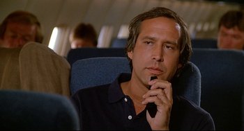 Movie still from “Fletch” (1985), directed by Michael Ritchie – A man sitting on a seat on an airplane; Close Up shot, Low angle