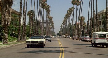 Movie still from “Fletch” (1985), directed by Michael Ritchie – Palm trees line a street lined with parked cars; Extreme Wide shot, Low angle