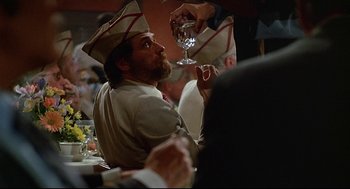 Movie still from “Fletch” (1985), directed by Michael Ritchie – A man sitting at a table with a glass of wine; Medium shot, Over the shoulder angle