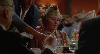 Movie still from “Fletch” (1985), directed by Michael Ritchie – An older woman wearing a hat sitting at a dinner table; Close Up shot, Over the shoulder angle
