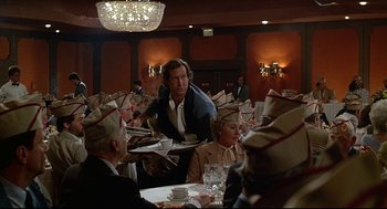 Movie still from “Fletch” (1985), directed by Michael Ritchie – A group of people sitting at a table with plates of food on it; Medium shot, Over the shoulder angle