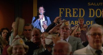 Movie still from “Fletch” (1985), directed by Michael Ritchie – A crowd of people watching a man sing a song in front of a crowd; Medium shot, Low angle