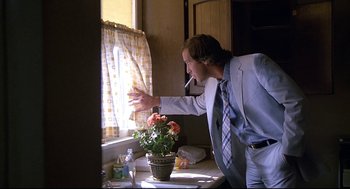 Movie still from “Fletch” (1985), directed by Michael Ritchie – A man standing in front of a window with flowers; Medium shot, Low angle