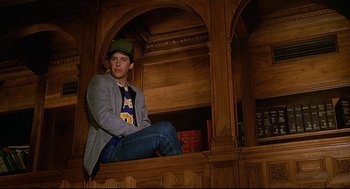 Movie still from “Fletch” (1985), directed by Michael Ritchie – A man sitting on top of a wooden shelf; Medium shot, Low angle