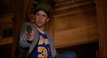 Movie still from “Fletch” (1985), directed by Michael Ritchie – A man sitting on the ground holding a remote control; Medium shot, Low angle