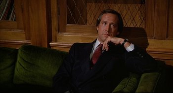 Movie still from “Fletch” (1985), directed by Michael Ritchie – A man sitting on a couch wearing a suit; Close Up shot, Low angle