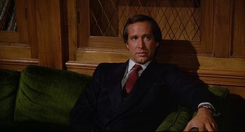 Movie still from “Fletch” (1985), directed by Michael Ritchie – A man in a suit and tie sitting on a couch; Close Up shot, Low angle