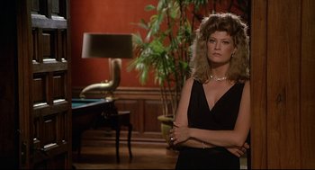 Movie still from “Fletch” (1985), directed by Michael Ritchie – A woman standing in a living room next to a desk; Medium shot, Over the shoulder angle