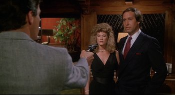 Movie still from “Fletch” (1985), directed by Michael Ritchie – A man taking a picture of a woman and a man in a suit; Medium shot, Over the shoulder angle