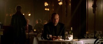 Movie still from “Flickering Lights” (2000), directed by Anders Thomas Jensen – A man sitting at a table with a glass of wine in front of him; Medium shot, Low angle