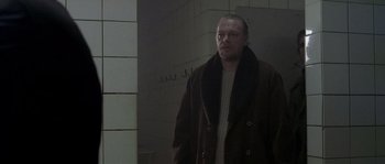 Movie still from “Flickering Lights” (2000), directed by Anders Thomas Jensen – A man in a brown coat standing next to a white wall; Medium shot, Over the shoulder angle