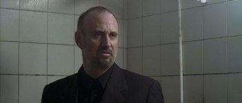 Movie still from “Flickering Lights” (2000), directed by Anders Thomas Jensen – A man in a black suit is standing in front of a tiled wall; Close Up shot, Low angle