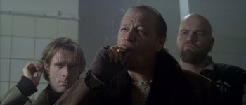 Movie still from “Flickering Lights” (2000), directed by Anders Thomas Jensen – A man smoking a cigarette while wearing a glove; Close Up shot, Low angle