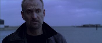 Movie still from “Flickering Lights” (2000), directed by Anders Thomas Jensen – A person wearing a jacket near a body of water; Close Up shot, Low angle