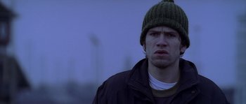 Movie still from “Flickering Lights” (2000), directed by Anders Thomas Jensen – A man wearing a green hat and a black jacket; Close Up shot, Low angle