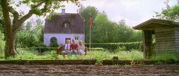 Movie still from “Flickering Lights” (2000), directed by Anders Thomas Jensen – Three people sitting on a bench in front of a house; Wide shot, Low angle